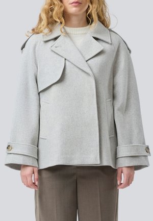 Hellgraue Wollmischjacke mit übergroßem Kragen, doppelter Knopfleiste, weiten Ärmeln und Knopfdetails. Getragen über einem cremefarbenen Pullover.