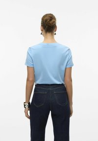 T-shirt azzurro chiaro a maniche corte con maniche arrotolate, abbinato a jeans aderenti a vita alta di un blu indaco scuro. Design semplice, tessuto morbido.