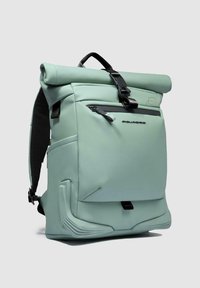 Mochila de color verde menta con tapa enrollable, correas ajustables, bolsillo frontal con cremallera y fondo texturizado para mayor estabilidad. Presenta elegantes acentos de hardware en negro.