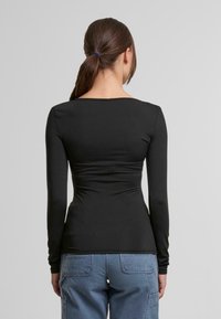 Černé dlouhé rukávy s výstřihem do kulata, přiléhavý střih, hladká textura a minimální švy. V kombinaci s světle modrými cargo kalhotami.