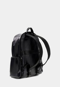 Sac à dos en cuir noir avec des bretelles réglables, une poche latérale et deux boucles à l'avant. Texture lisse avec un design épuré.
