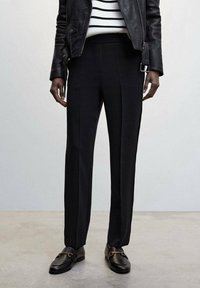 Sorte skræddersyede bukser med en tætsiddende pasform, der har en glat tekstur og rene linjer. Sammen med sorte læder mokkasiner og en stribet bluse.