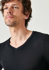 Black V-neck t-shirt made of smooth, stretchy fabric. Close-fitting design with short sleeves and a clean neckline, highlighting a minimal style.