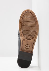 Semelle de chaussure noire avec un tread en caoutchouc marron. Conçue avec un motif de grip texturé et un logo circulaire. Bords épurés et matériaux durables.