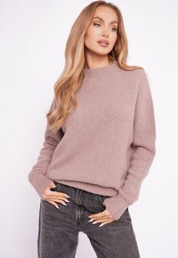 Jasnoróżowy sweter z kaszmiru z wysokim kołnierzem i długimi rękawami, zestawiony z ciemnoszarymi dżinsami. Gładka faktura, minimalistyczny design.