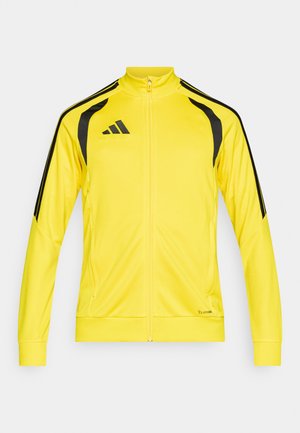 Żółta kurtka zapinana na zamek, wykonana z materiału syntetycznego, z czarnymi akcentami na ramionach i bokach. Posiada wysoki kołnierz i dwie kieszenie.