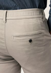 Pantalones gris claro con una tela suave, que cuentan con un bolsillo trasero cosido y un botón negro. La cinturilla tiene detalles elásticos para mayor comodidad.