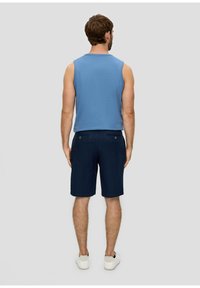 Un débardeur bleu sans manches et un short noir marine avec deux poches arrière, porté avec des baskets blanches. Le tissu semble lisse avec une coupe décontractée.