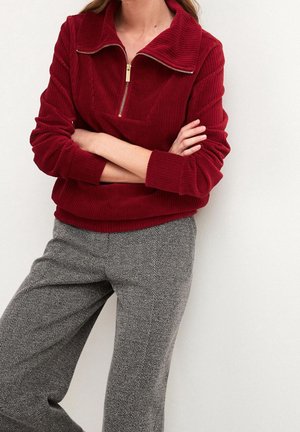 Bordeaux corduroy pullover met een hoge kraag en een gouden rits. Gepaard met grijze broek met visgraatpatroon. Zachte textuur, relaxte pasvorm.