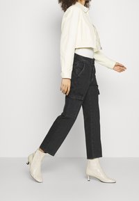 Zwarte cargobroek met zijzakken, gecombineerd met een strakke witte top en een cropped crèmekleurige jack. Draagt crèmekleurige enkellaarsjes met een lage hak.