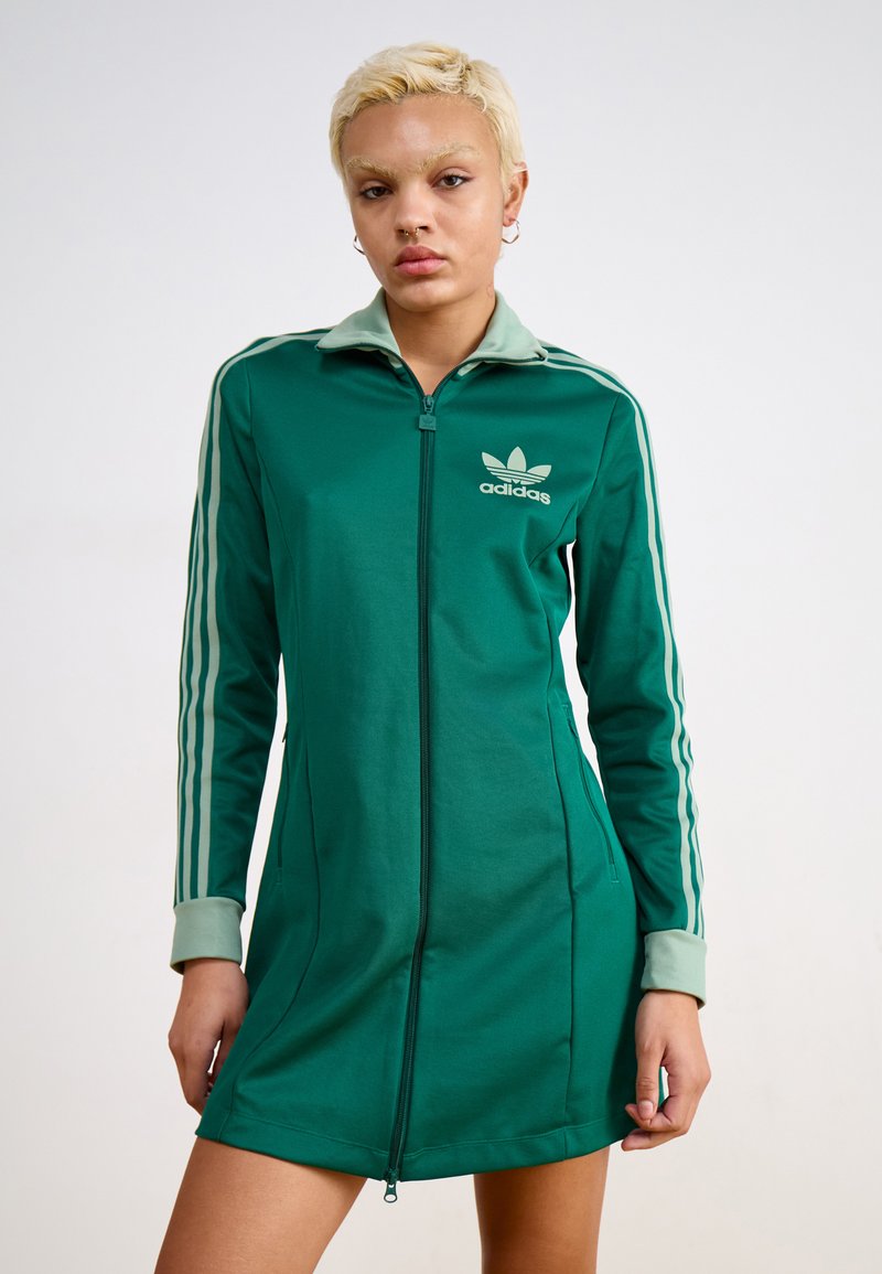 Roheline Adidasist lahtise tõmblukuga kleit, mis on valmistatud siledast kangast, millel on kõrge krae, pikad varrukad ja valged kolme triibu aktsendid varrukatel.