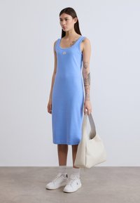 Φόρεμα γαλάζιο με ριπ ύφασμα και στρογγυλή λαιμόκοψη, που φτάνει μέχρι τα μέσα της γάμπας. Συνδυάζεται με λευκά αθλητικά παπούτσια και κρέμ τσάντα ώμου. Απλός σχεδιασμός.