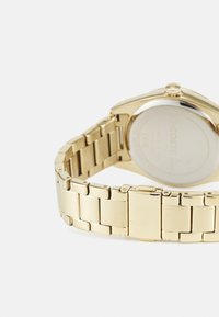 Reloj de pulsera de metal dorado con pulsera de eslabones. El reloj cuenta con una caja redonda y un acabado liso y brillante. La parte trasera es plateada y transparente.