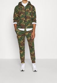 Hooded camouflage sweatshirt och matchande joggare i gröna och bruna nyanser, med dragkedjestängning, fickor och ribbade manschetter.