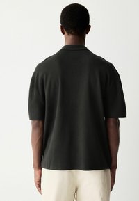 Polo de manga corta en gris oscuro, hecho de una tela suave, con un cuello clásico y un corte relajado, con un diseño liso y sin costuras.