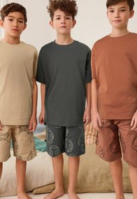 Trei chlapci sú oblečení v ležérnom oblečení s tričkami s krátkym rukávom v béžovej, tmavošedej a medenej farbe, doplnenými o vzorované šortky v zladených farbách.