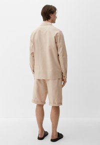 Jasno beżowa lniana koszula z podwiniętymi mankietami, zestawiona z dopasowanymi szortami. Prosty krój, gładka faktura i luźny fason.