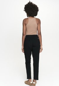 Czarne dresy z elastycznym pasem, zestawione z beżowym topem na ramiączkach. Dresy mają zwężający się krój i są wykonane z miękkiego, lekkiego materiału.