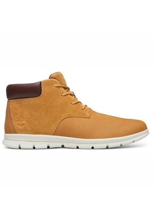 Bottines en daim marron avec semelle en caoutchouc blanc, présentant un bout rond, un laçage à l'avant et un accent en cuir marron sur le talon.