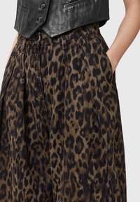 Hlače širokih nogavica s leopardovim vzorcem v rjavi in črni, izdelane iz teksturirane tkanine, z stranskimi žepi in nagubanimi detajli.