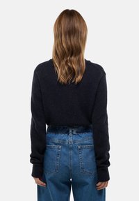 Pull sombre bleu marine à manches longues et poignets côtelés, associé à un jean bleu taille haute avec une coupe décontractée et deux poches arrière.