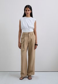 Haut blanc sans manches avec taille froncée, associé à un pantalon large beige taille haute. Des sandales noires à brides complètent la tenue.