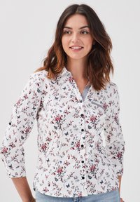 Chemise blanche à manches longues avec un imprimé floral et de papillons en rouge et bleu foncé, dotée d'un col classique.