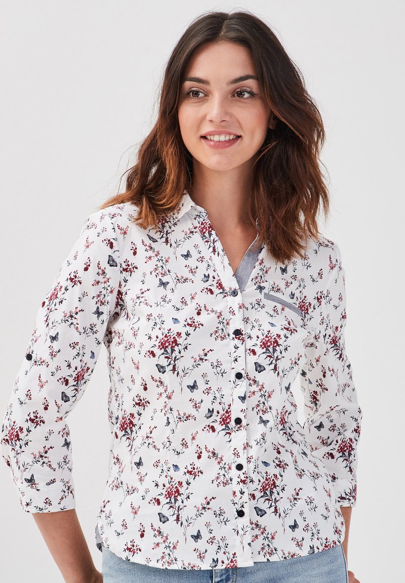 Chemise blanche à manches longues avec un imprimé floral et de papillons en rouge et bleu foncé, dotée d'un col classique.