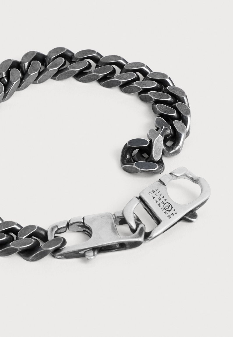 Pulsera de cadena gruesa de plata con un cierre único que presenta números grabados y un cierre seguro de gancho sobre un fondo liso.