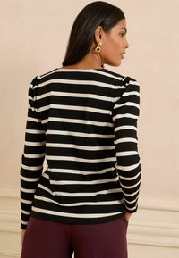Chemise à rayures noires et blanches à manches longues avec des détails de manches bouffantes, en tissu doux, encolure ronde, associée à un pantalon violet uni.
