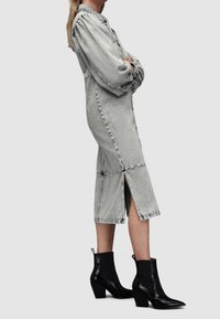 Harmaa farkkukangas midi-mekko, jossa on pitkät hihat, rypytetty olkapää ja etuhalkio, yhdistetty mustiin nilkkureihin, joissa on kapeneva kärki ja lohkopohja.