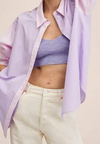 Hellviolettes, gestreiftes, übergroßes Hemd mit hochgekrempelten Ärmeln, darüber ein lavendelfarbenes Strick-Crop-Top, kombiniert mit cremefarbenen Hosen.