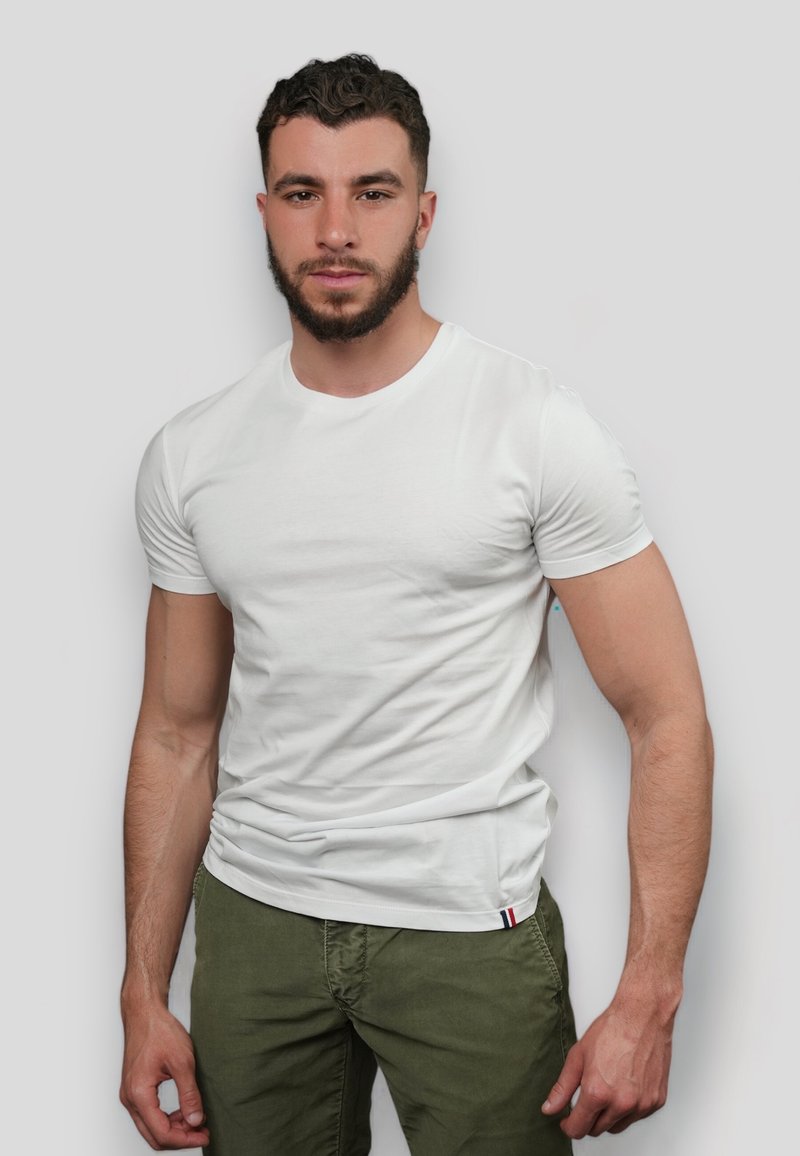 T-shirt en coton blanc avec un col rond, des manches courtes et un design légèrement ajusté ; présente une petite accentuation rouge, blanche et bleue à l'ourlet.
