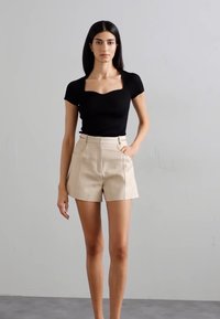 Zwarte aangesloten top met korte mouwen en vierkante halslijn, gecombineerd met hoge beige shorts met een taillerapport en voorzakken.