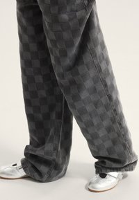 Pantaloni in denim grigio a quadri con vestibilità ampia, abbinati a scarpe argento lucide con cinturino e accento nero.