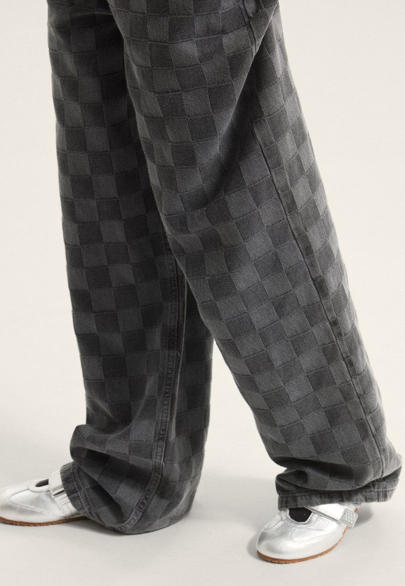 Pantaloni in denim grigio a quadri con vestibilità ampia, abbinati a scarpe argento lucide con cinturino e accento nero.