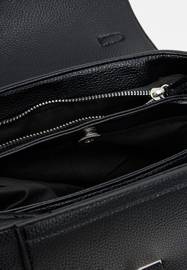 Intérieur d'un sac à main en cuir noir avec une finition texturée, comportant une poche zippée et une doublure en tissu lisse. Les accents incluent du matériel en ton argent.