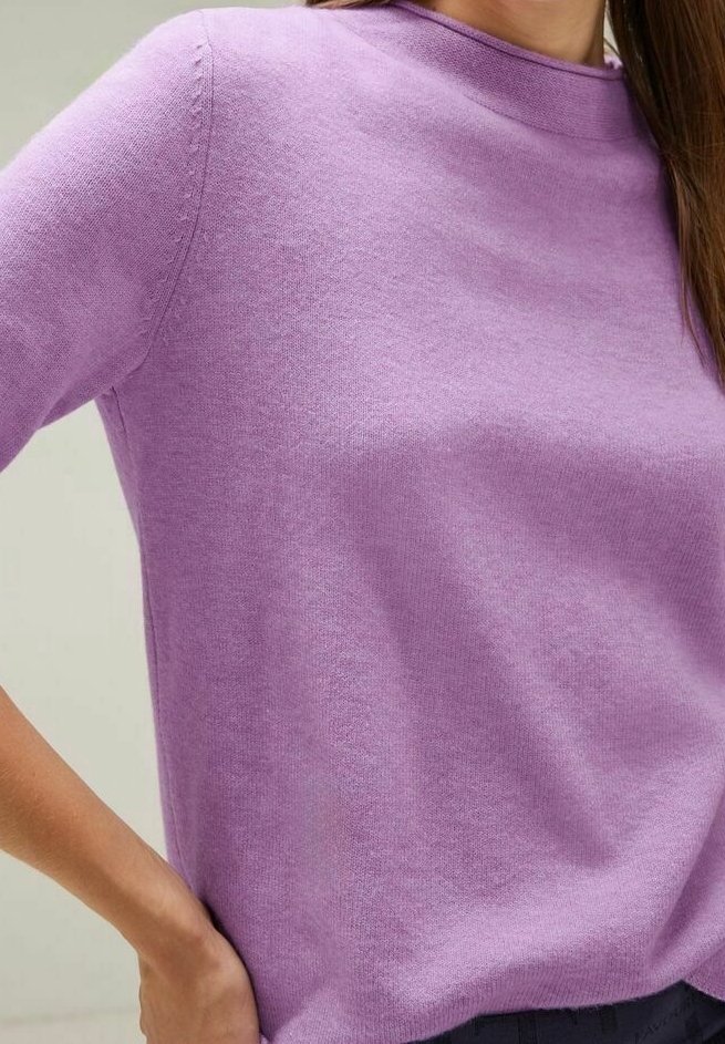 Lila stickad tröja med rund hals och trekvartslånga ärmar, med en mjuk textur och subtila ribbmönster längs sömmarna.
