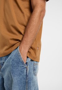 Brun bomulds t-shirt med rund halsudskæring, korte ærmer og et sideskilt. Parret med lyseblå denim shorts med en lomme.