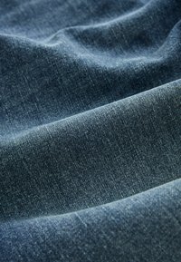 Material de denim de culoare albastru închis, cu o textură netedă și modele subtile în diagonală, cu nuanțe variate ce creează adâncime și dimensiune.
