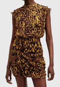 Ärmlös mini-klänning med rynkor i gult och svart leopardmönster samt små silverdetaljer, bärs av en person mot en ljus bakgrund.