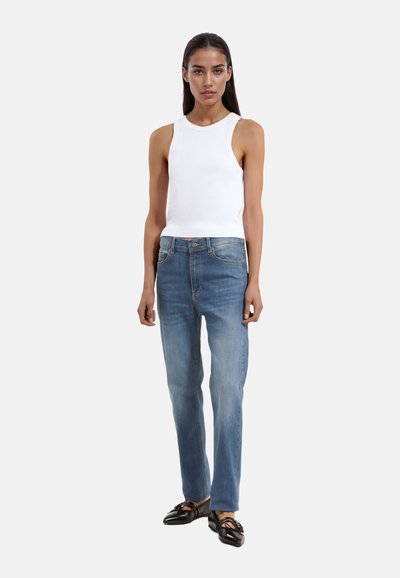 Witte geribde tanktop, lichtblauwe recht-toe recht-aan jeans en zwarte instappers. Eenvoudig ontwerp, soepele stof en klassieke silhouet.