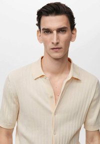 Short-sleeve shirt in light beige with vertical ribbed texture, soft fabric, and a classic collar. Features a button front closure.