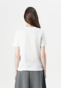 White cotton t-shirt with short sleeves, round neckline, and a smooth texture, paired with a grey skirt. Clean, minimalist design.