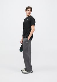 Μαύρο βαμβακερό μπλουζάκι με λογότυπο στο στήθος, σε συνδυασμό με γκρι φόρμα με πλαϊνές τσέπες και λογότυπο Puma. Φορεμένο με ανοιχτόχρωμα αθλητικά παπούτσια.