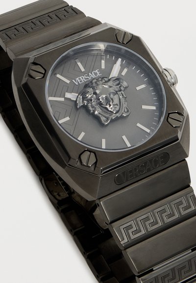Μαύρο ρολόι χειρός Versace με τετράγωνο καντράν, λογότυπο Medusa στο κέντρο, ασημένιους δείκτες ώρας και μεταλλικό βραχιόλι με σχέδιο και λογότυπο Versace.