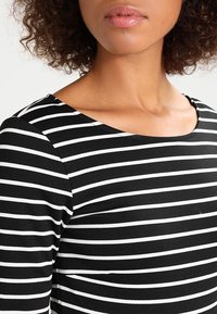 Haut à rayures noir et blanc avec un décolleté arrondi et une texture douce, présentant des rayures horizontales de largeurs variées sur le tissu.