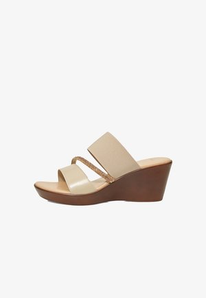 Des sandales compensées beige présentent deux bretelles en élastique, dont une ornée de paillettes, et une lanière en cuir lisse au niveau des orteils. Talon compensé marron texturé.