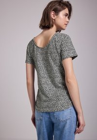 T-shirt nera a maniche corte con motivo floreale bianco, scollatura posteriore rotonda e silhouette aderente, abbinata a jeans blu.