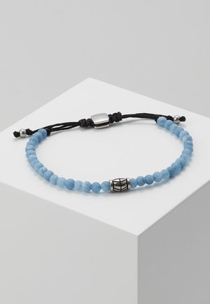 Bracelet ajustable avec de petites perles rondes bleues, une perle centrale argentée avec des lignes noires, un cordon noir et des fermoirs argentés sur une surface blanche.